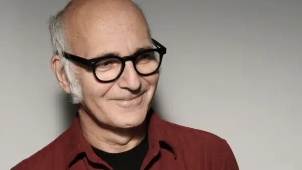 Retrato de Ludovico Einaudi, músico italiano. Su edad se refleja en su mirada serena y su cabello canoso. Viste una camisa roja.