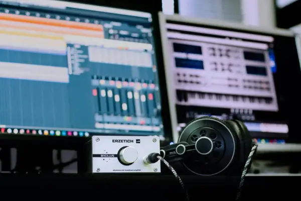 Estudio de **audio digital** con monitores mostrando software de producción musical, un amplificador de auriculares y auriculares negros.