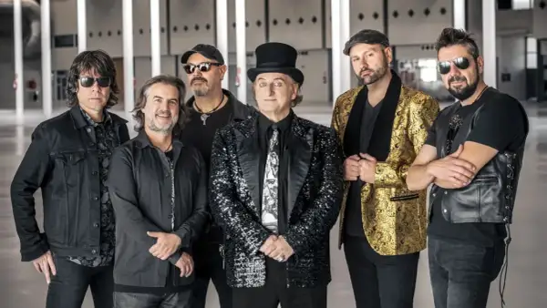 Los miembros de la Orquesta Mondragón posan juntos, listos para un concierto. El cantante principal lleva un sombrero de copa y un traje brillante.