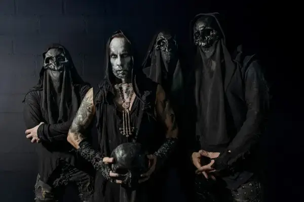 Cuatro figuras encapuchadas, con máscaras de calavera y maquillaje facial pálido, posan sombríamente. El líder sostiene un cráneo, evocando la estética de grupos black metal.