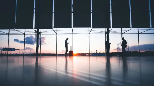 Siluetas de personas con maletas en un aeropuerto al atardecer. Quizás buscando ofertas en **que es ticketswap** para su próximo viaje.