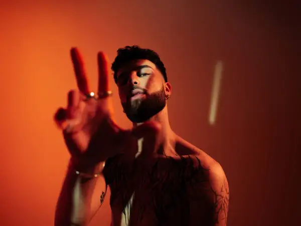 Joven con tatuajes y barba hace el signo de la paz. ¿Oguz DJ de dónde es?
