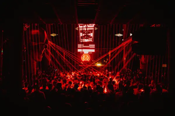 Multitud vibrante en un club nocturno, bañada en luces rojas. El logo de "Circus Nation" ilumina el escenario.